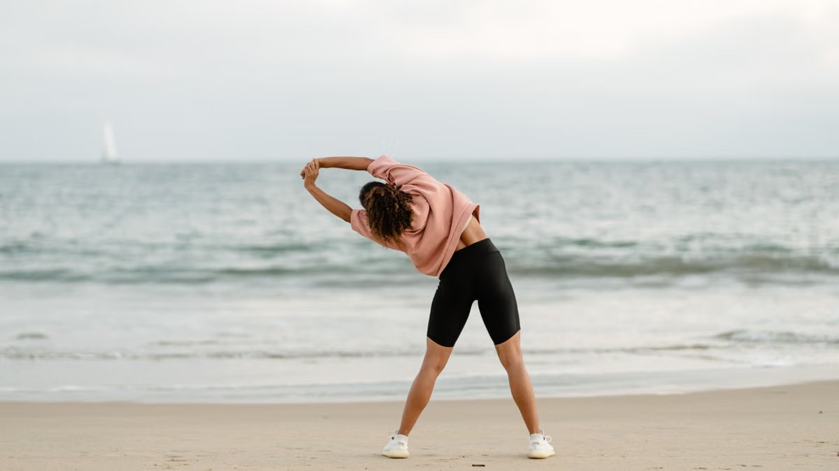 A woman stretching on the beach with a scenic ocean view at sunrise.